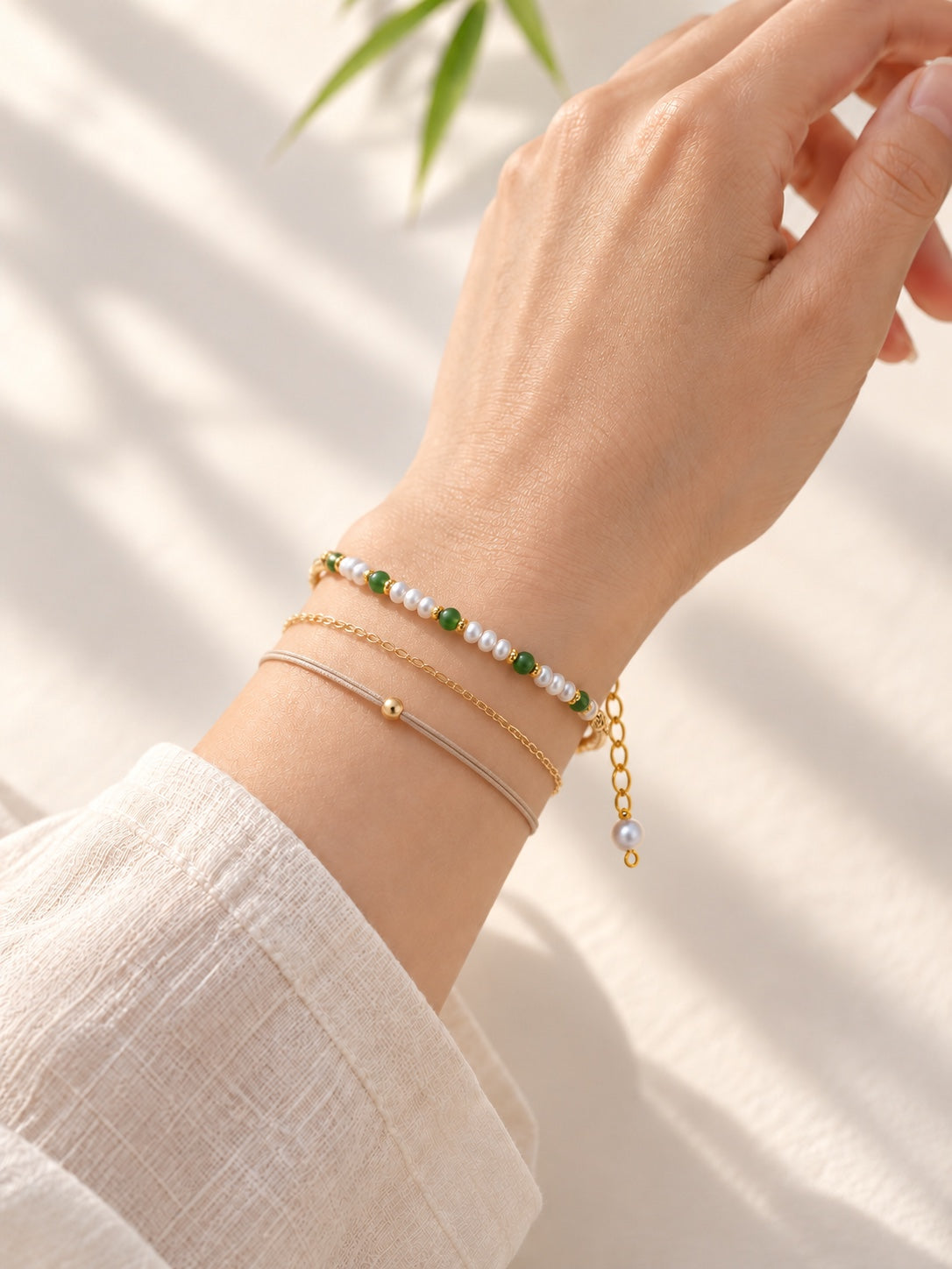 Green jadeite and freshwater pearl bracelet styled with additional chain and cord bracelets; other bracelets not included