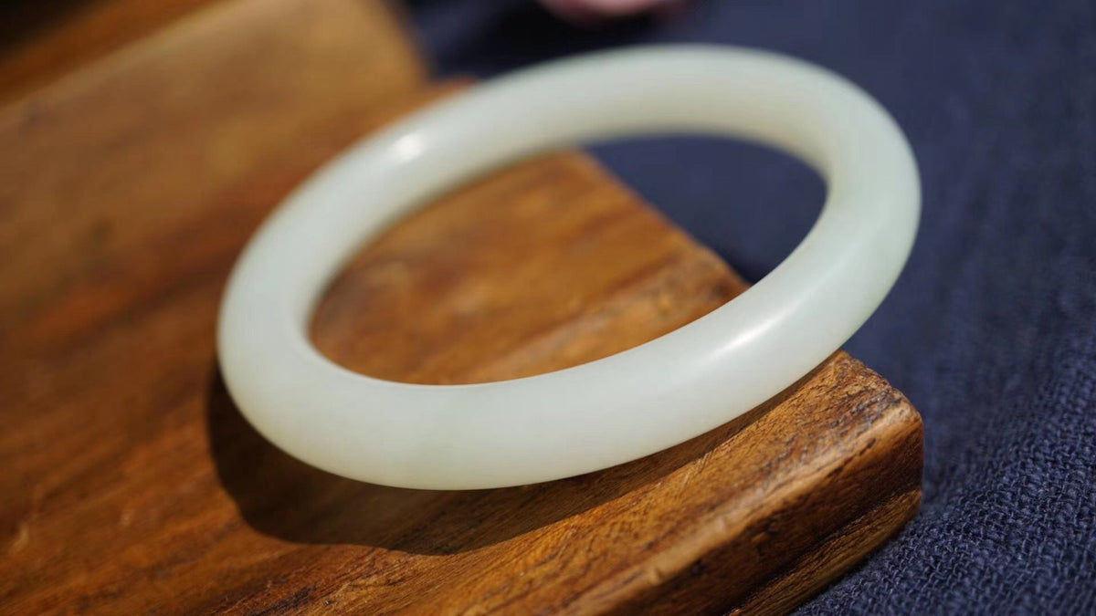 A pale jade bangle resting on warm wood