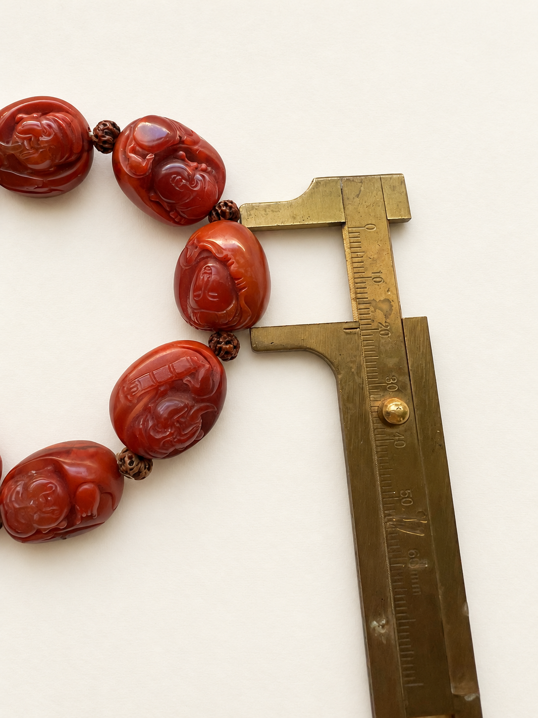 Close view of a carved Nanhong agate bead beside a brass caliper.