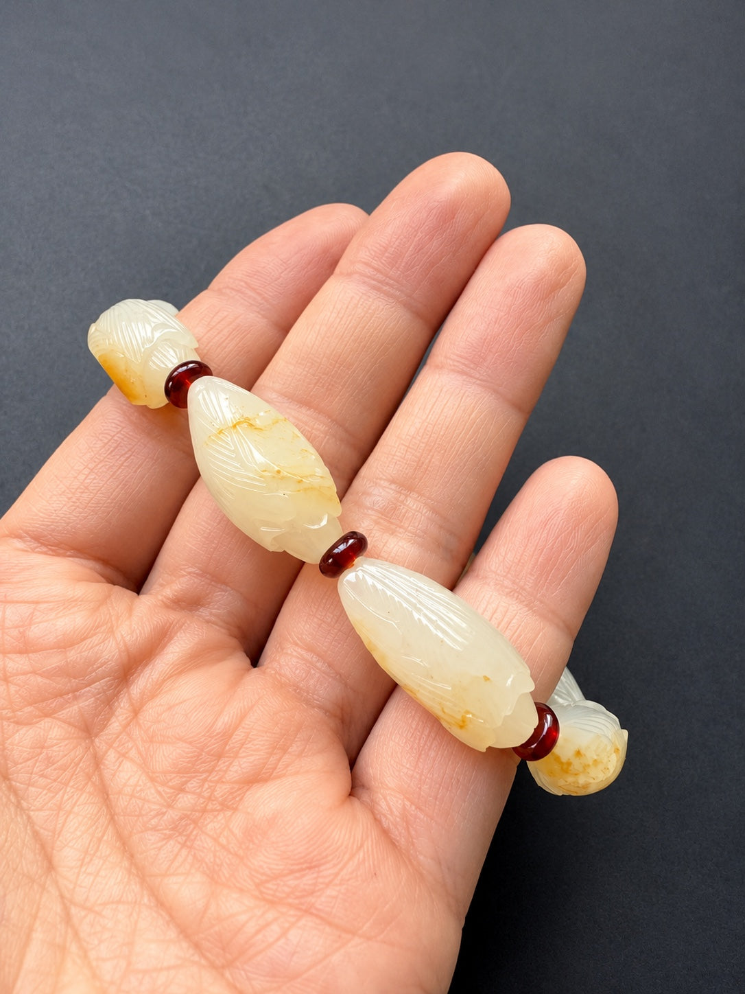 Nephrite jade magnolia bud bracelet held in a hand to show carving and scale