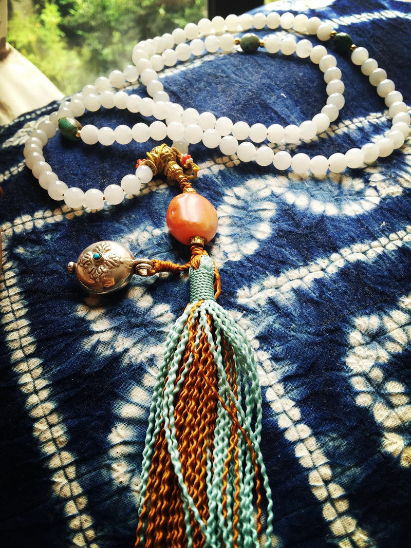 A strand of white beads with a colorful tassel on blue patterned fabric, from the founder’s archive.