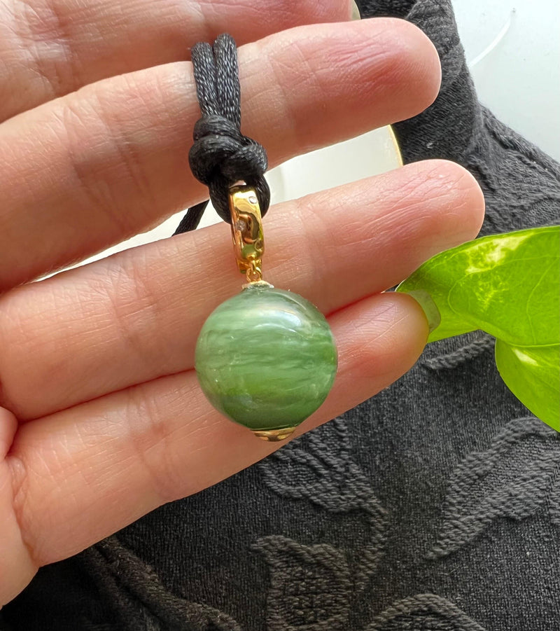 A finished green stone pendant held in the hand.