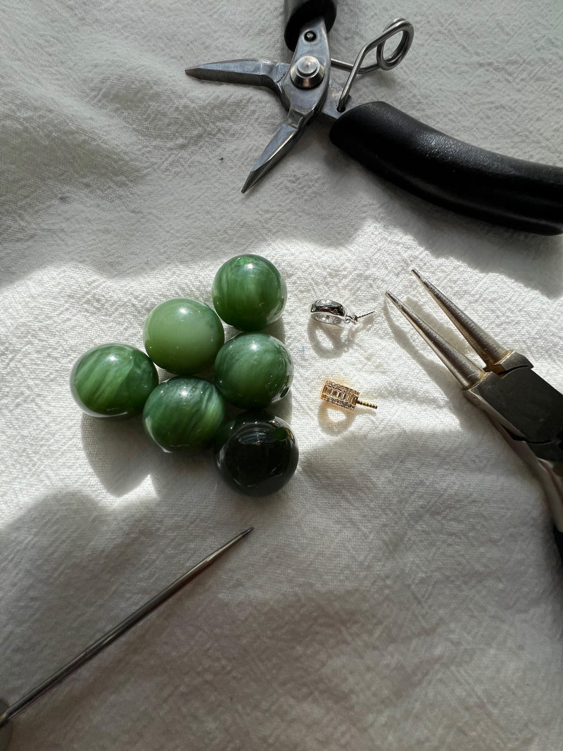 Green stone beads, jewelry findings and tools on a work surface.